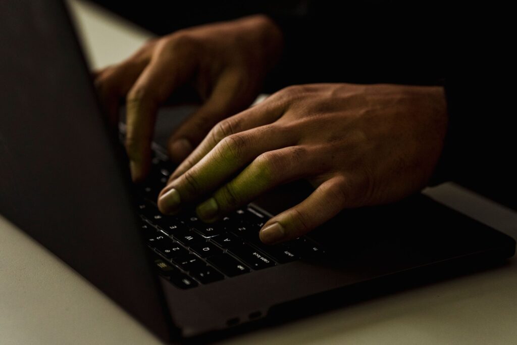 A close-up view of hands typing on a laptop keyboard in a dimly lit environment. Photo by Sora Shimazaki on Pexels.